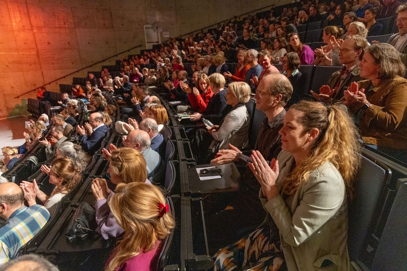 Een zaal vol mensen die applaudisseren na de voordracht.