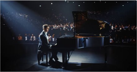 Een pianist speelt op een vleugel op een groot podium, in het licht van een spot, voor een volle zaal.