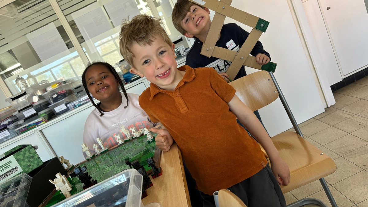 Drie kinderen in de plusklas tonen trots hun zelfgemaakte schaakspel en kartonnen molen.