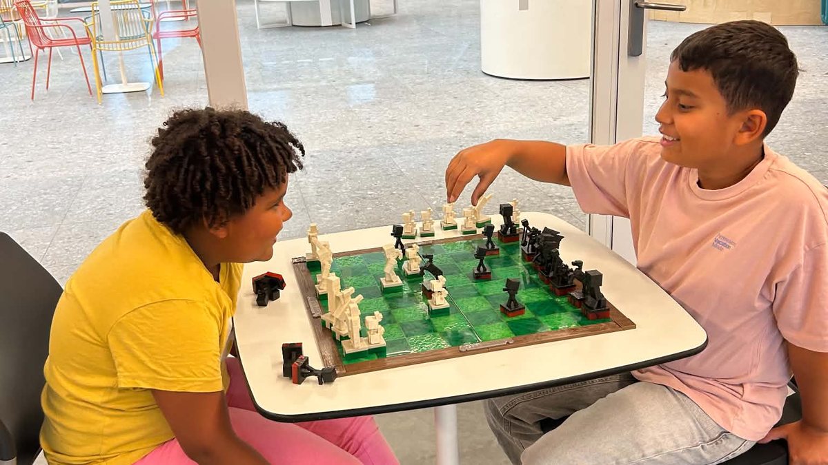 Twee kinderen spelen samen een zelfgebouwd schaakspel in de lichte hal van T2 Campus.