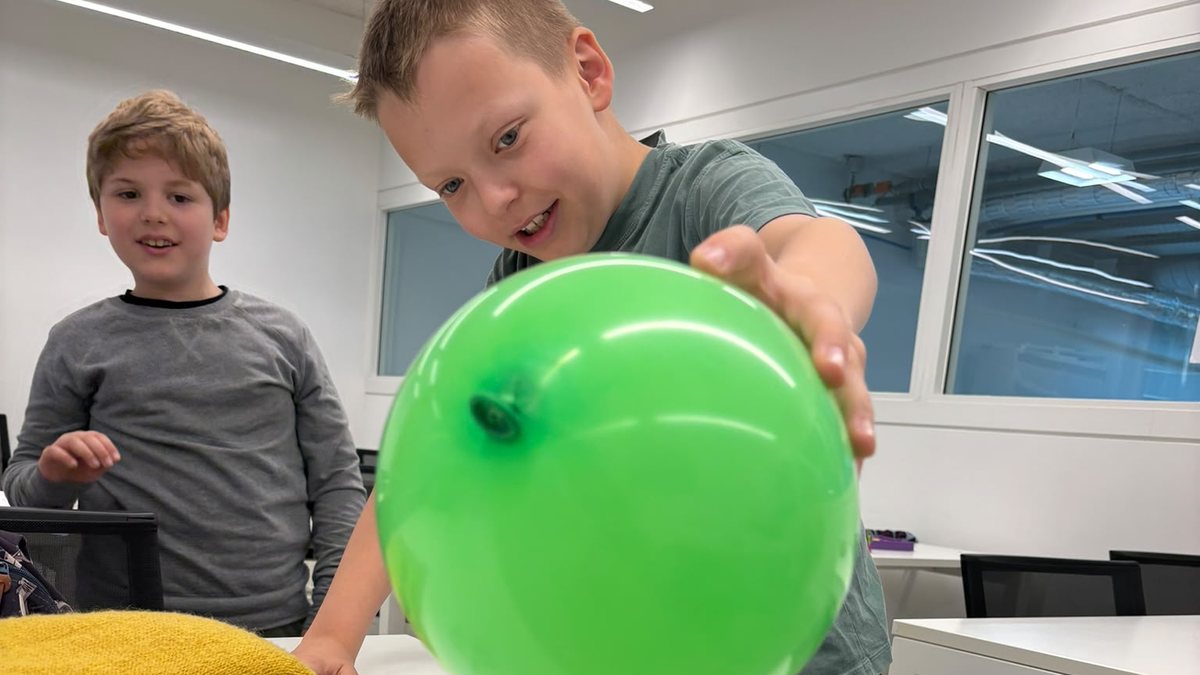 Een kind houdt een groene ballon boven een tekening tijdens een proefje met statische elektriciteit.