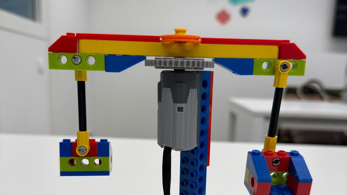 Een zelfgebouwde constructie van lego met een motor, een tandwiel en twee bakjes die op en neer gaan.