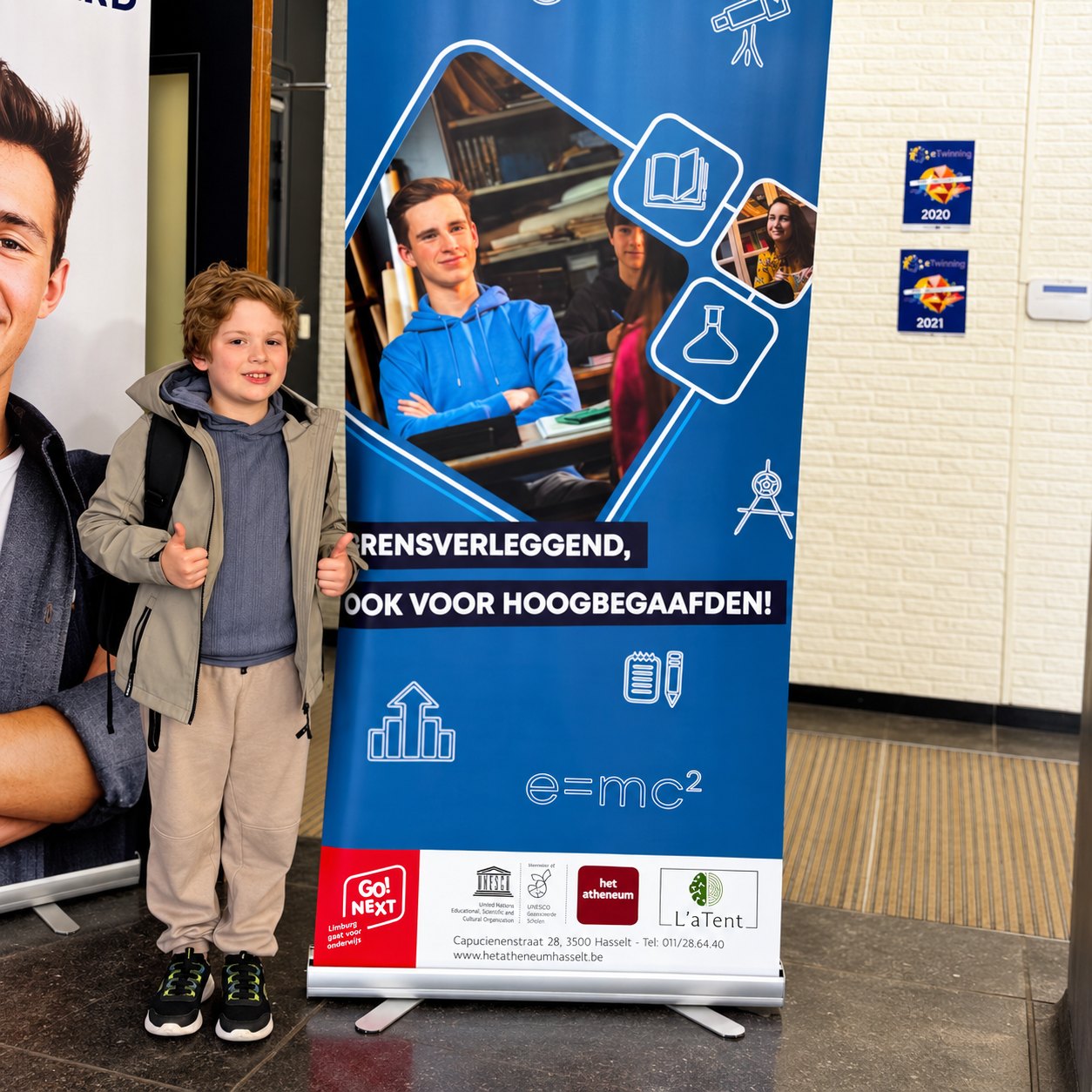 Kind steekt twee duimen op naast een banner van het atheneum