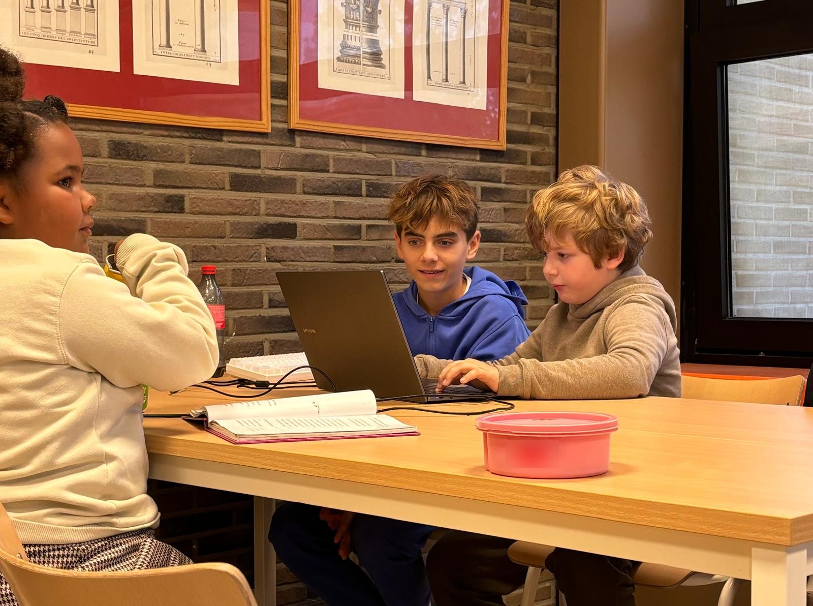 Een oudere en een jongere jongen werken samen op een laptop, een meisje zit naast hen aan tafel