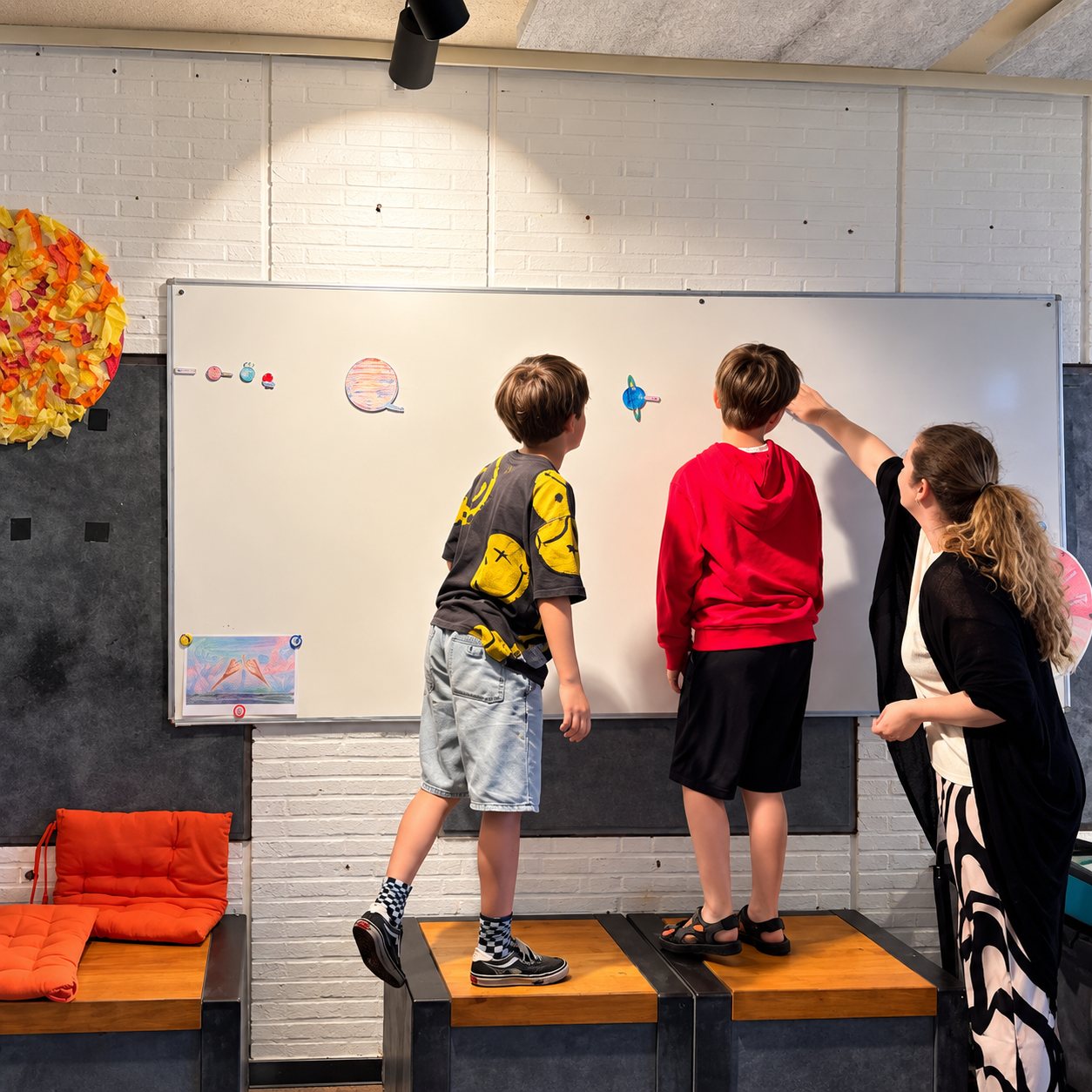 Kinderen hangen planeten op het bord met een begeleider